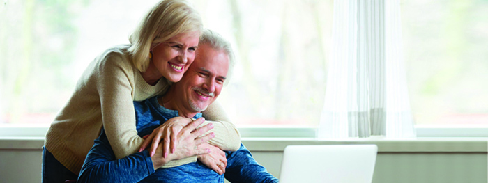 Woman hugs man as they both look at a laptop computer screen.