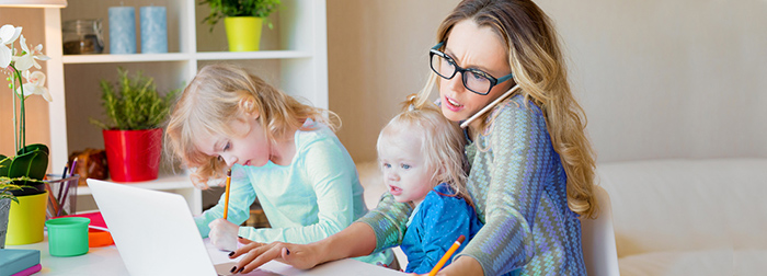 Busy mom working from home with toddler in her lap and grade-school-age daughter beside her.